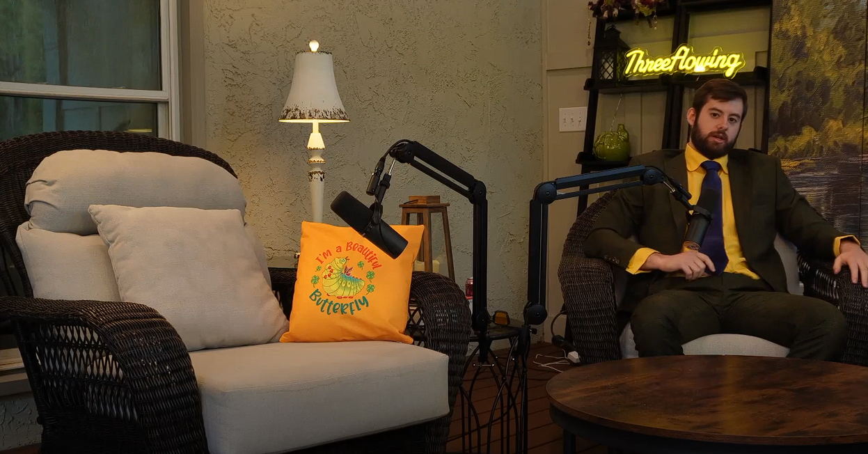 ThreeFlowing podcast host in a suit with the neon sign in background
